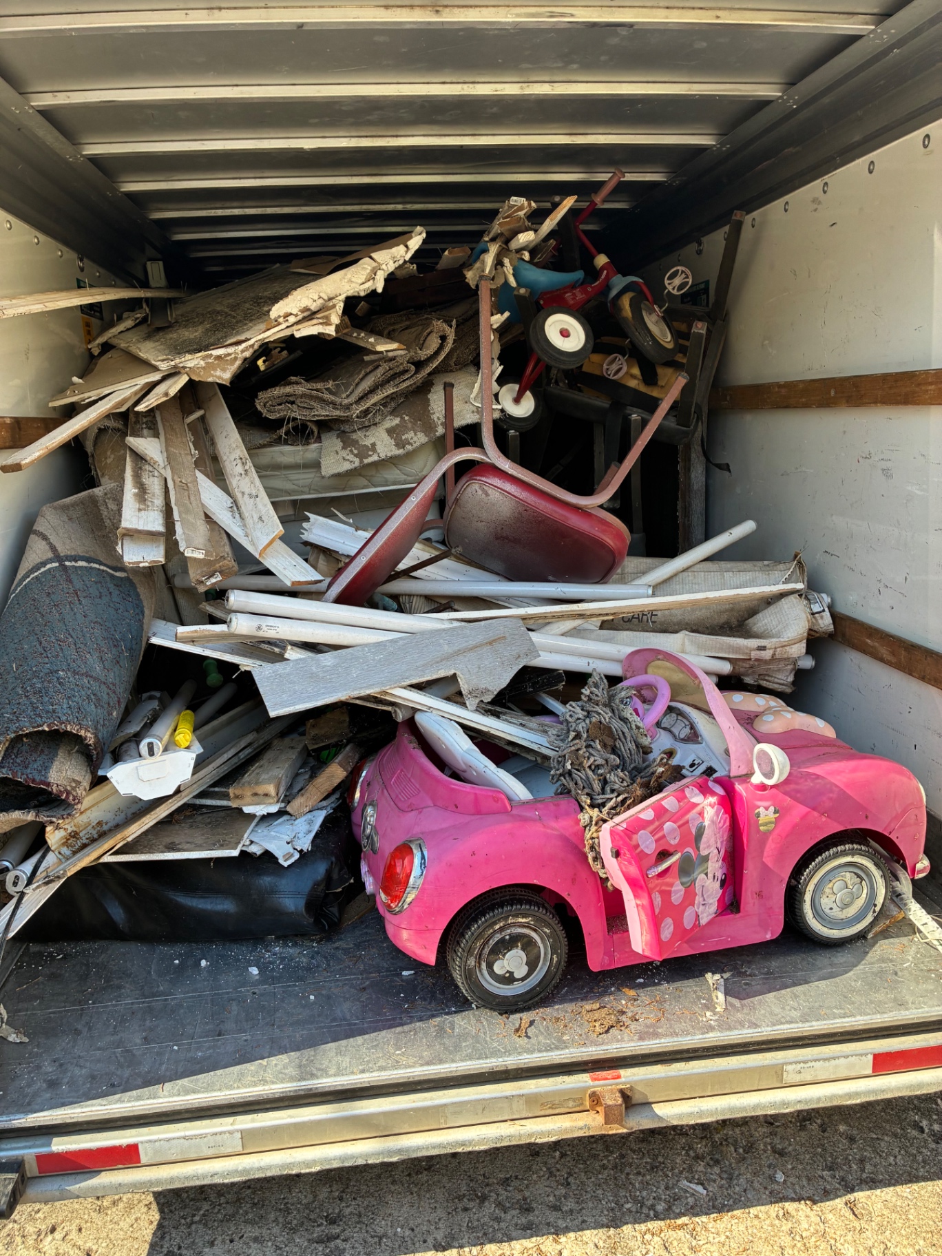 Trailer loaded with household junk, scrap wood, and a child’s toy car